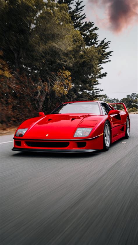 a red sports car is driving down the road with trees in the backgroud