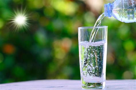 Hand pouring water into a glass cup with a bokeh nature background ...