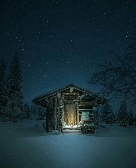 a cabin in the snow at night with lights on and stars above it's roof