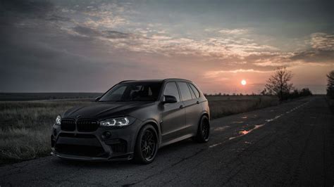 the bmw x5 is parked on the side of the road in front of the setting sun