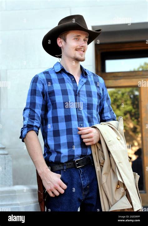 Handsome young man, wearing cowboy hat and carrying a coat, smiles at ...