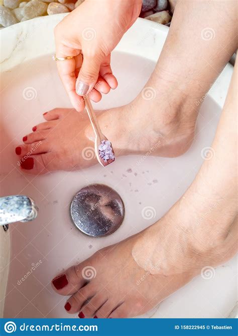 Hand Pouring Epsom Salt from Small Wooden Spoon and Female Feet in Foot ...