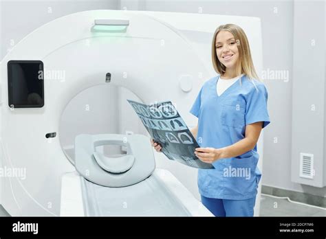 Happy young blond female radiologist in blue uniform analyzing x-ray ...