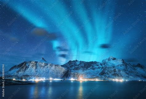 Aurora borealis over the sea, snowy mountains and city lights at night ...