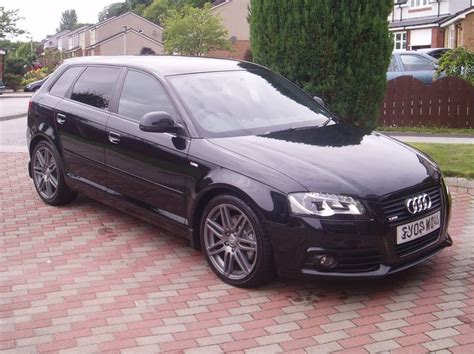 a black car parked in front of a tree on a brick driveway next to houses