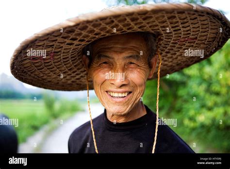 A Chinese farmer wears a traditional conical hat and smiles to the ...