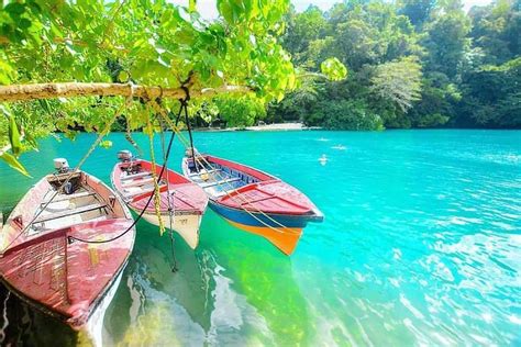 two boats are tied to the dock in front of some trees and blue lagoon water