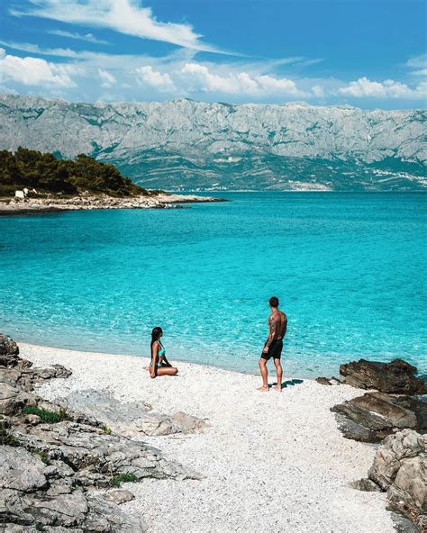 two people are standing on the beach in front of clear blue water and ...