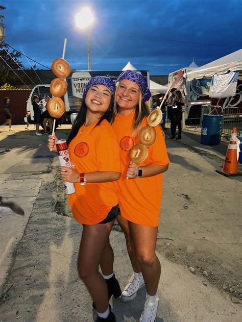 two women in orange shirts holding donuts and drinking sodas while ...