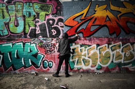 Image of Teenage graffiti artist spray painting a wall - Austockphoto