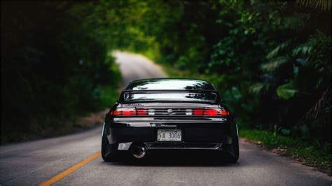 the back end of a black sports car driving down a tree lined road in ...