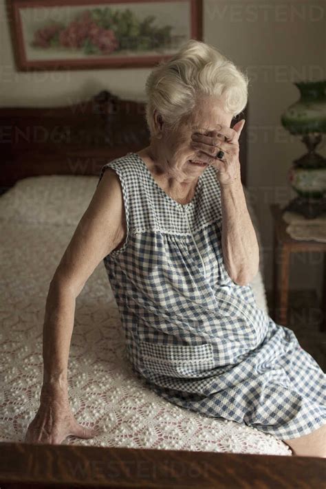 Sad older woman crying on bed stock photo