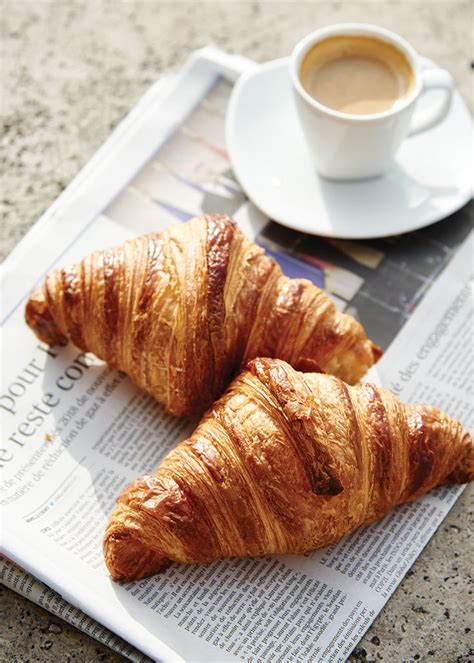 two croissants sitting on top of a newspaper next to a cup of coffee