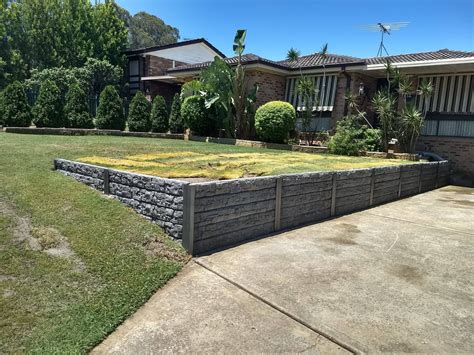 a stone retaining wall in front of a house with grass and bushes on the ...