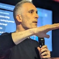 A middle-aged white man on stage with a microphone gesticulating as he stares into the future.