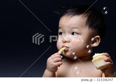 Cute asian baby boy is eating french fries and cake with both hi 31539247