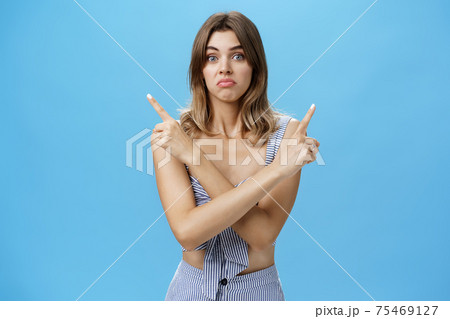 Help girl make hard decision. Portrait of gloomy unsure hesitant cute female model with natural hair and tan crossing hands over body pointing at upper right and left corners with sad uncertain look 75469127