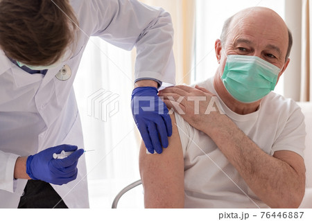 Doctor vaccinating senior male patient at home. 76446887