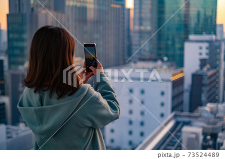 高層ビルの夕景を撮影する女性 73524489