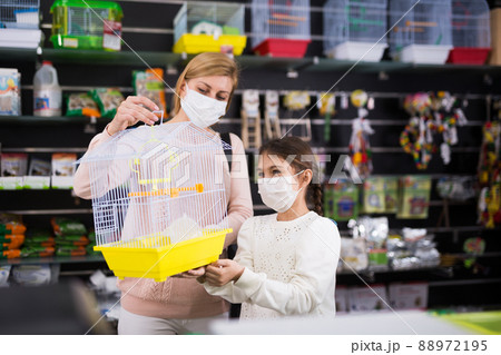 Mother with her daughter in masks choosing bird cage 88972195