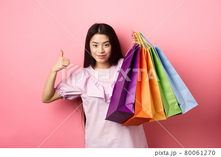 Shopping. Stylish girl showing colorful paper bags and thumbs-up, recommend store discounts, standing against pink background 80061270