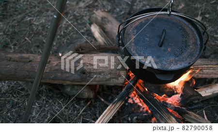 Camping outdoors in nature. Cooking pot hanging over a campfire on a tripod at a tourist camp, a bowler on a bonfire by firewoods. Preparing dinner in a pot in the forest. Nice camping background 82790058