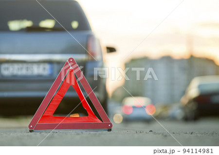 Red emergency triangle stop sign and broken car on a city street. 94114981