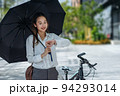 Cute Asian business woman with holding black umbrella looking at watch outdoors on sunny day 94293014