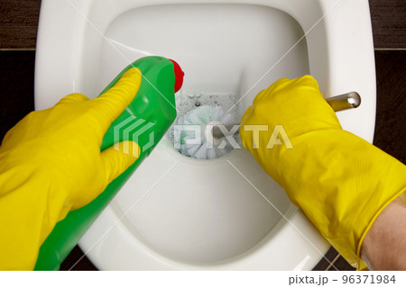 Toilet cleaning and disinfection. Cleaner in yellow rubber gloves cleans the toilet bowl with a brush and disinfectant 96371984