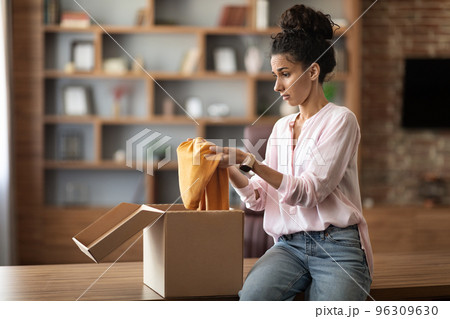 Sad dissatisfied young female looking at clothes, unpacking parcel 96309630