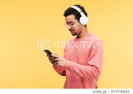 Young man in headphones and pink pullover scrolling through playlist 97476682