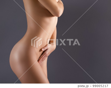 Naked, skin and nude woman in studio posing against a background with her smooth body. Young and sensual person covering breast with hand or sexy, beautiful and natural model with a tan 99005217