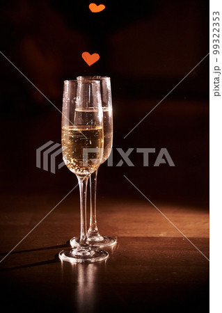 Two glasses of champagne, which stand on a black background with a beautiful bokeh, glasses against the background of hearts, the concept of Valentine's day, romantic dinner. Copy space. High quality 99322353