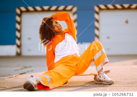 Young African American woman - dancer dancing in the street at sunset. Stylish woman with curly hair in an orange suit showing some moves 105266732