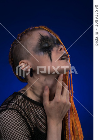 Headshot of woman with eyes closed, orange color braids hairdo, spooky stage make up painted on face 108913590