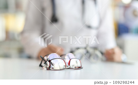 Ophthalmologist sits in background with various glasses for fitting lenses in frame 109298244