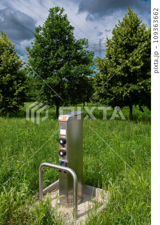 Charging Station For Electric Cars In Green Meadow In Front Of Trees And Electricity Cables 109363662