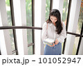 Young woman standing near the glass door and looking down at some notebooks 101052947