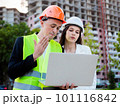 Young male builder and female engineer explain and check the construction and repair of a multi-storey building. House on construction site, outdoors. 101116842