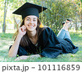 Young smiling female student in black graduate gown lies on the grass in the university park 101116859