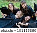 Several young smiling female students in black graduation gowns lie on the grass in the university park 101116860