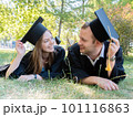 Happy guy and girl look at each other lying on the lawn in a black graduate gown and an academic cap of the university 101116863