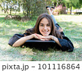 Portrait of a happy smiling girl in a black robe lying on the grass. A young woman is celebrating her graduation. New life 101116864