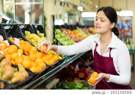 Female grocery store worker lays out ripe tangerines on counter and display case 103158569