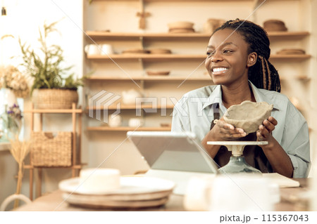 Contented african american woman showing a clay jar to the audience on online workshop 115367043