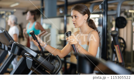 Portrait of sporty woman doing cardio workout on elliptical cross trainer at fitness center 115305522