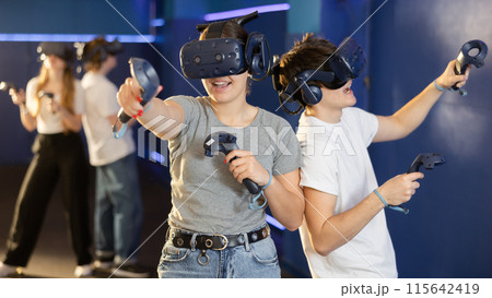 Portrait of woman using virtual reality goggles controlling joysticks standing in dark room 115642419