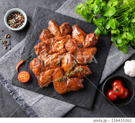 Roasted chicken wings bbq with tomato and fresh herb on a black slate on a dark background. 116433262