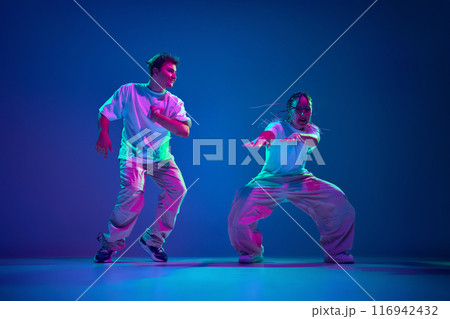 Burst of energy. Artistic young performers, man and woman dancing hip-hop, showing skills of modern dance against purple studio background in neon light 116942432