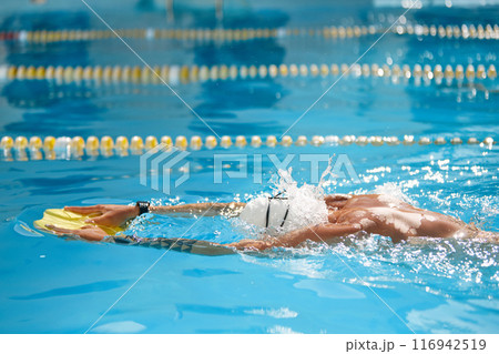 Sporty man wearing white cap and goggles cuts through water with precision, fully immersed in his outdoor practice. 116942519